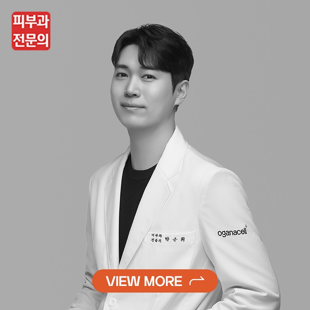 Professional portrait of a young man in a white blazer against a gray background, facing forward with a calm smile; orange View More button overlays the lower chest.